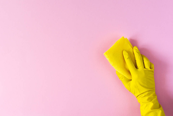 Ruka ve žluté gumové rukavici s čisticí houbou na růžovém pozadí - Fotografie, Obrázek