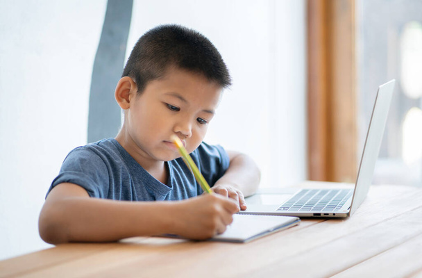Aasialainen poika oppii verkko-opetusta kotona digitaalisella tabletilla ja tekee koulun kotitehtäviä. Lapsi hakee tabletilla tietoa internetistä, verkko-oppiminen verkko-opiskelua. - Valokuva, kuva
