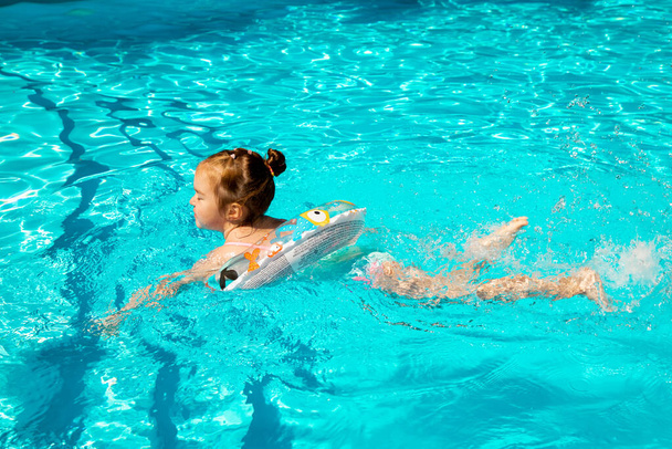 Досить маленька дівчинка грає з надувним кільцем у відкритому басейні в спекотний літній день. Діти вчаться плавати
. - Фото, зображення