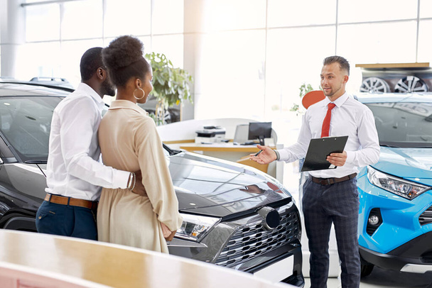 friendly salesman and beautiful couple in car showroom - Photo, Image