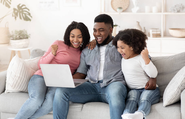 Lotteria online. Eccitato afro-americano famiglia di tre celebrando la vittoria con il computer portatile - Foto, immagini