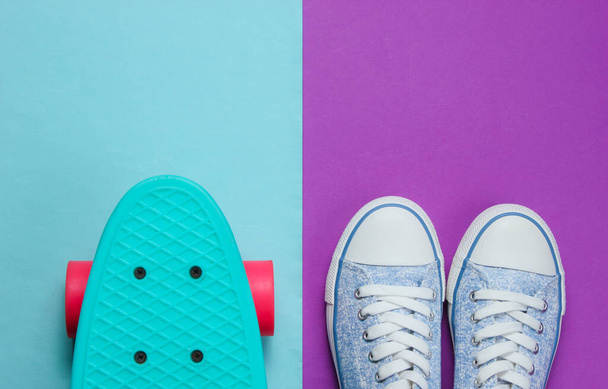 Хіпстерські кросівки та вид зверху скейтборду на фіолетово-блакитному тлі. Концепція мінімалізму моди
. - Фото, зображення