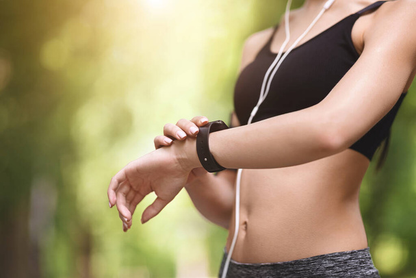 Femme athlète méconnaissable vérifiant les indicateurs de bracelet de fitness tout en faisant du jogging à l'extérieur, gros plan - Photo, image