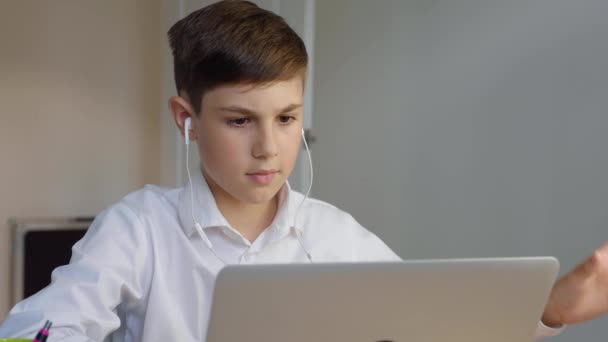 Koulupoika kuulokkeissa kannettavan tietokoneen avulla online-koulutukseen kotona. Poika tykkää tehdä koulun läksyjä netissä. Nuori poika liikemies työskentelee kannettavan tietokoneen ja juo kahvia - Materiaali, video
