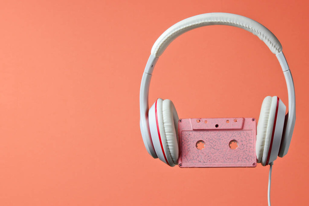 White classic wired headphones with audio cassette isolated on coral color background. Retro style. 80s. Minimalistic music concept. - Foto, immagini