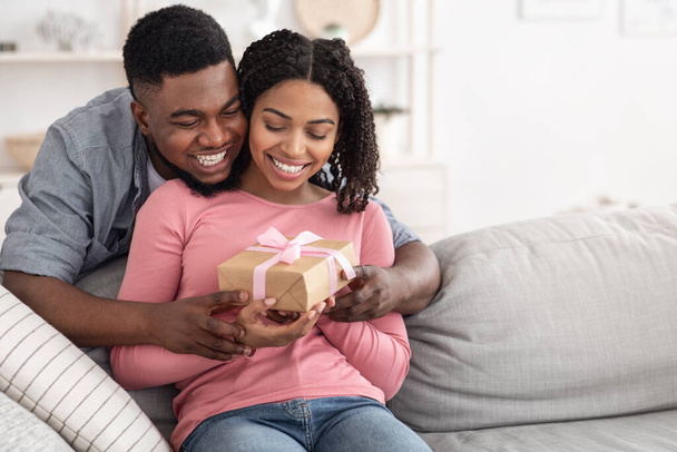 Romanttinen yllätys. Rakastava musta aviomies antaa lahjan onnelliselle vaimolle kotona - Valokuva, kuva