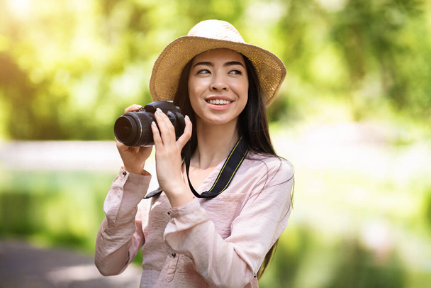 Outdoor Hobbies. Happy asian woman traveler taking photo with modern camera - Foto, afbeelding