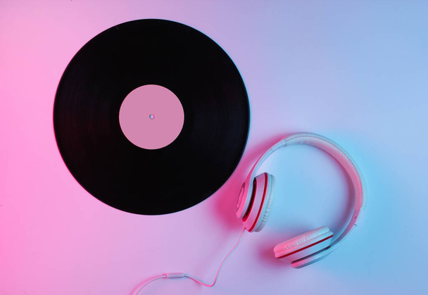 Концепція музики в стилі ретро. Класичні навушники, вініловий запис з градієнтним рожево-блакитним неоновим світлом. Поп-культура. 80-ті роки. Вид зверху
 - Фото, зображення