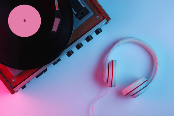 Retro style music concept. Classic headphones, vinyl record player with gradient pink-blue neon light. Pop culture. 80s. Top view - Photo, Image