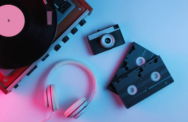 Flat lay retro 80s pop culture objects. Vinyl player, headphones, video tapes, film camera with gradient neon blue-pink light. Retro wave.  Top view - Photo, Image