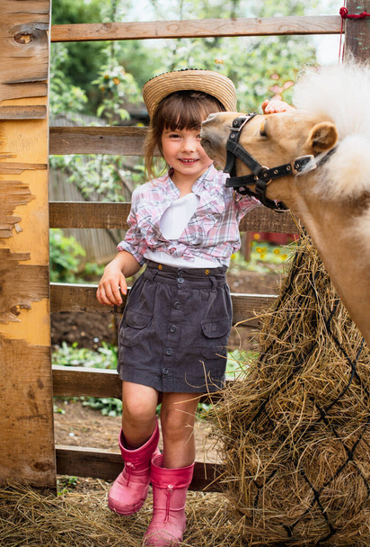 Blond hair girl in cowboy hat and plaid shirt with pony little horse summertime - Foto, immagini