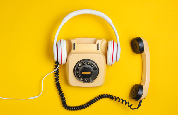 Estilo retro creativo plano laico. Teléfono vintage giratorio con auriculares blancos clásicos sobre fondo amarillo. Cultura pop. Vista superior - Foto, imagen
