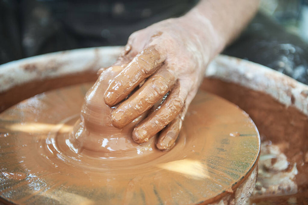 The potter makes pottery dishes on potter's wheel. The sculptor in workshop makes clay product closeup. Hands of the potter.  - Foto, immagini
