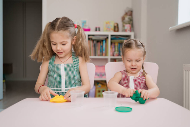 Cute little girls moulding from plasticine on pink table - Фото, изображение