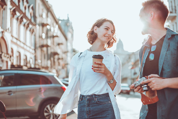 Una joven pareja de turistas hipster con una cámara retro están hablando entre sí mientras caminan por la ciudad. Historia de amor romántica - Foto, imagen