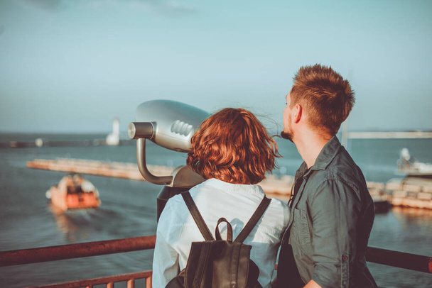 Jeune couple amoureux regarde à travers les jumelles de la ville à la station de la mer. Promenade romantique dans une ville inconnue - Photo, image