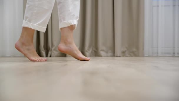 Jeune femme avec sa fille marche pointe des pieds nus sur un sol en bois chaud à la maison - Séquence, vidéo