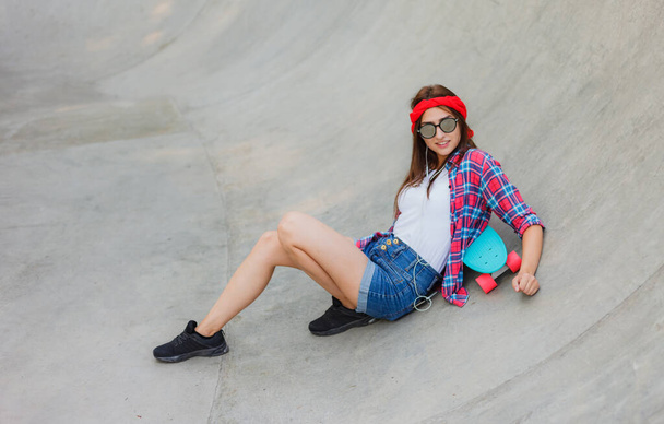 Le passe-temps des jeunes. Jeune femme hipster reposant avec une planche à roulettes dans un skatepark - Photo, image