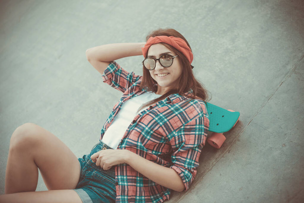 Pasatiempo juvenil. Joven mujer hipster descansando con un monopatín en un skatepark - Foto, Imagen
