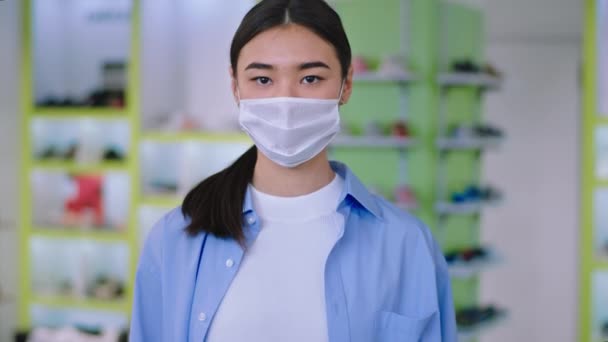 Asian young woman with a protective mask portrait looking straight to the camera concentrated she is in a shop. 4k - Footage, Video