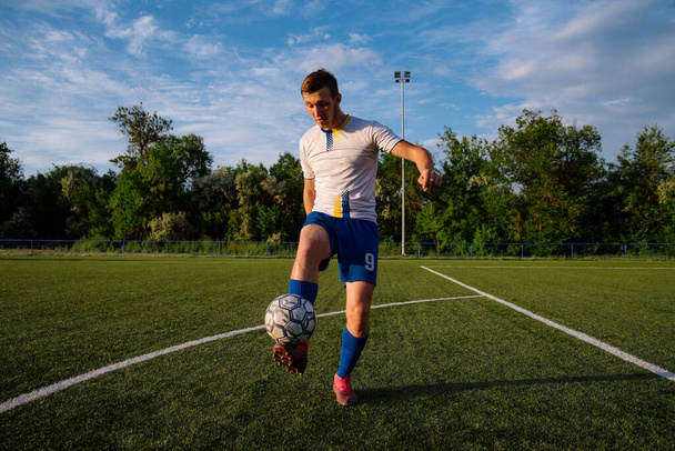 Young male soccer player juggles a ball on a soccer field.Athlete juggling the football with his feet in stadium.Football sports concept - Фото, зображення