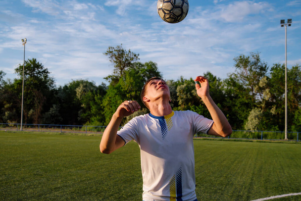 Young male soccer player juggles a ball on a soccer field.sport, football and people - soccer player playing and juggling ball using header technique on field.Football sports concept - Foto, Bild