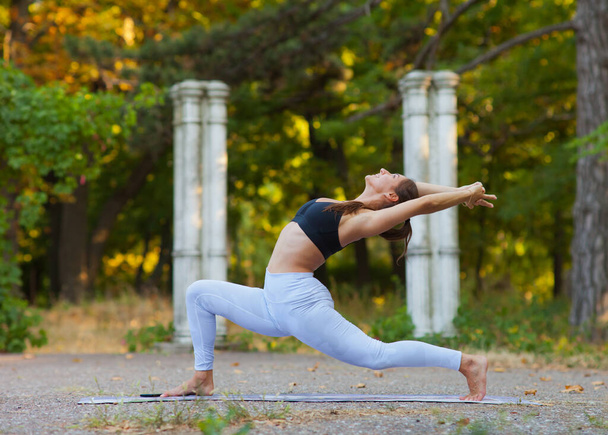 Joga i kondycja. Młoda kobieta ćwiczy równoważenie jogi poza domem. Ćwiczenia gimnastyczne w parku. - Zdjęcie, obraz