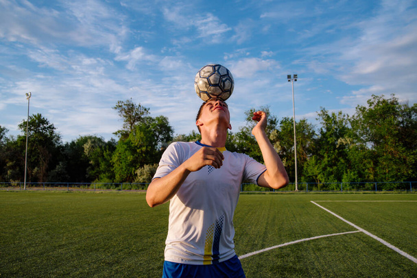 Young male soccer player juggles a ball on a soccer field.sport, football and people - soccer player playing and juggling ball using header technique on field.Football sports concept - Photo, Image