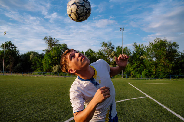 Young male soccer player juggles a ball on a soccer field.sport, football and people - soccer player playing and juggling ball using header technique on field.Football sports concept - Foto, imagen