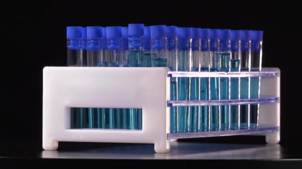Kísérleti csövek kék folyadékkal forgó fekete alapon egy laboratóriumban 4K - Felvétel, videó