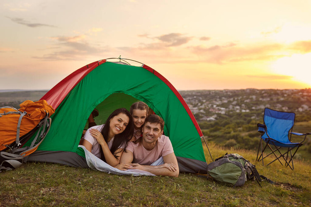 Onnellinen perhe lapsen kanssa telttaretkellä rentoutumassa sisällä teltassa. Huolehtivat vanhemmat ja heidän tyttärensä rentoutuvat leirintäalueella - Valokuva, kuva