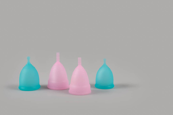 Set of four blue and pink menstrual cups on grey background with copyspace for text or creative presentation. Women health and zero waste concept. Female hygiene period products, alternative lifestyle - Photo, Image