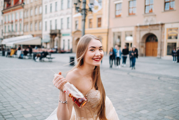 A bride in a wedding dress with long hair and a drink bottle in the Old town of Wroclaw. Wedding photo shoot in the center of an old Polish city.Wroclaw, Poland. - 写真・画像