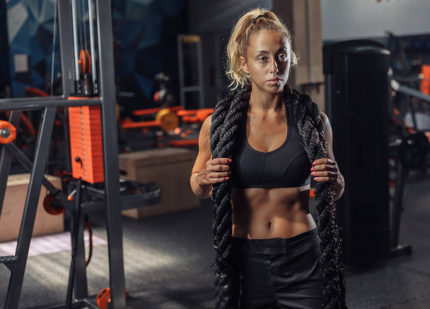 Young sport woman in sportswear with battle rope on her neck in the gym. Functional training. Healthy lifestyle concept - Photo, Image
