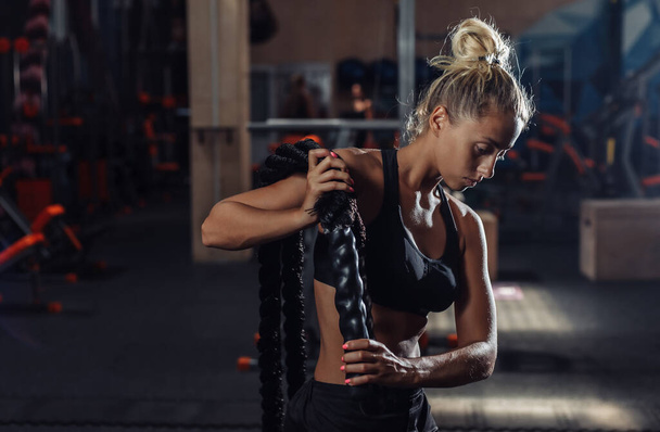 Young sport woman in sportswear is training with battle rope on her shoulders in the gym. Functional training. Healthy lifestyle concept - Foto, imagen