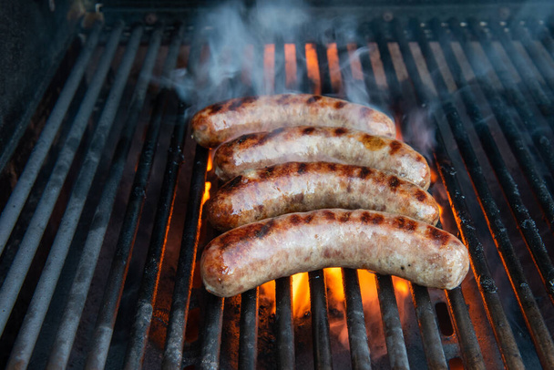 Brats being cooked on a grill with flame and smoke. - Photo, Image