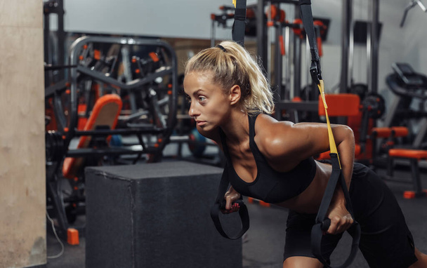 Young attractive sport woman in sportswear is training with fitness straps in the gym. Functional Training Concept - Photo, Image