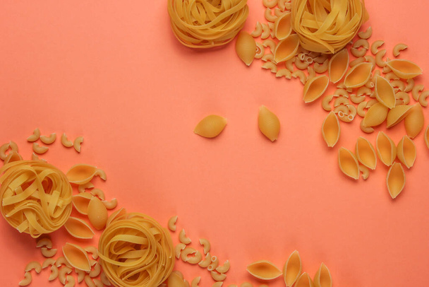Verschillende soorten rauwe Italiaanse pasta op koraal kleur achtergrond. Bovenaanzicht. - Foto, afbeelding