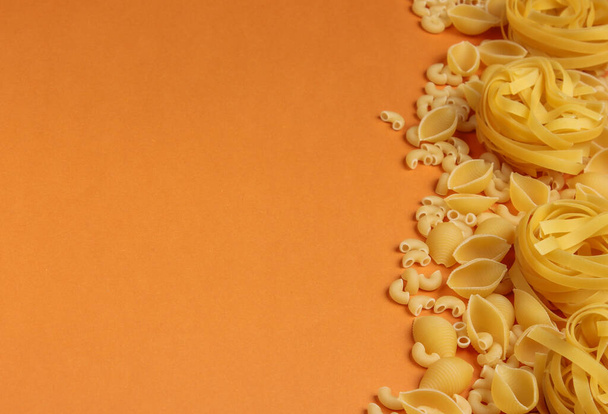 Verschillende soorten rauwe Italiaanse pasta op bruine achtergrond. Bovenaanzicht. Kopieerruimte - Foto, afbeelding