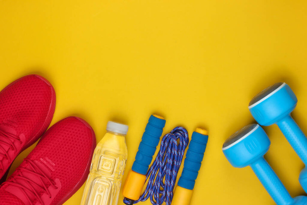 Equipment for training on yellow background. Sports shoes, skipping rope, dumbbells, bottle of water. Flat lay style. Top view. Copy space - Photo, Image