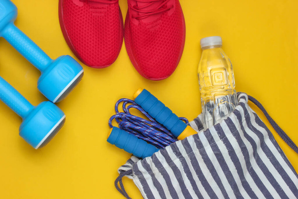 Gestreifte Sporttasche mit Sportoutfit und roten Turnschuhen auf gelbem Hintergrund. Sportliches Stillleben. Ansicht von oben. - Foto, Bild