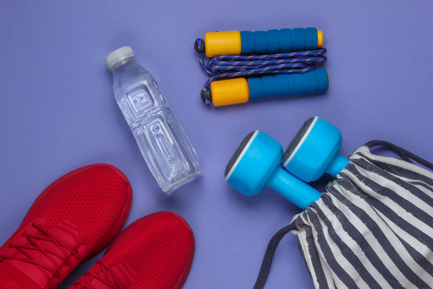 Striped sports bag with sports outfit and red sneakers on purple background. Sports still life. Top view. - Photo, Image