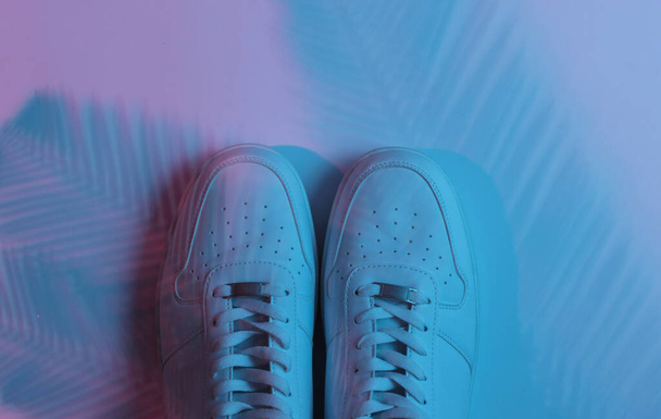 Stylish hister white sneakers on background with shadow from palm leaves. Neon gradient light. Top view - Photo, Image