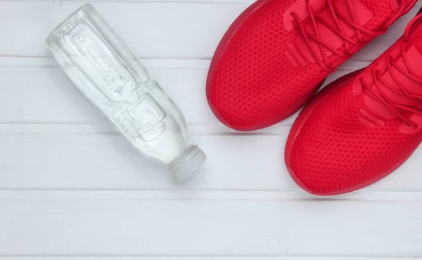 Красная спортивная обувь для бега, бутылка воды на белом деревянном полу. Вид сверху
. - Фото, изображение