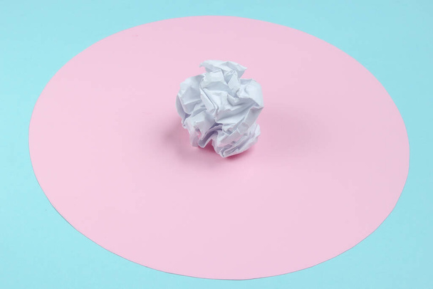 Zmačkaný papírový míč na modrém pozadí s růžovým pastelovým kruhem. Minimalistické podnikání zátiší. - Fotografie, Obrázek