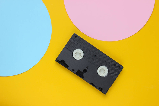 Cassette vidéo sur fond jaune avec cercle pastel rose bleu pour l'espace de copie. Vue de dessus. Concept rétro minimaliste. 80 ans. - Photo, image