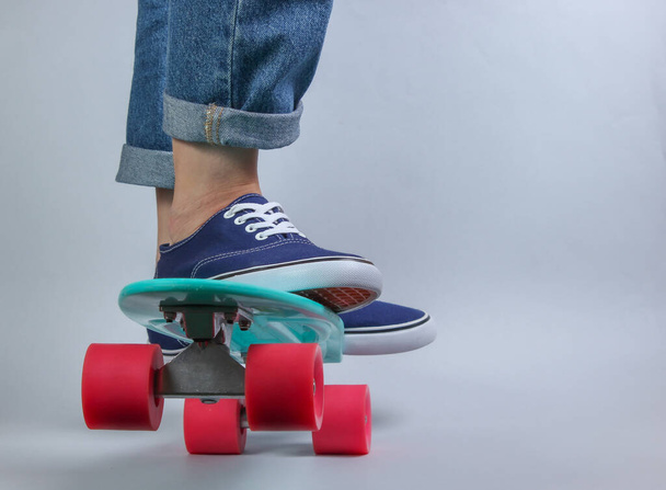 Youth hipster concept. Female legs in jeans and sneakers on cruiser board in the studio on white background. Summer fun - Foto, Imagem