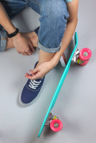 Youth hipster concept. Female legs in jeans and sneakers sitting on white background with cruiser board. Top view - Photo, Image