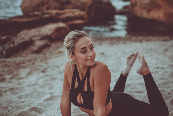 Jovem mulher bonita esporte em sportswear praticando exercício asana na areia na praia selvagem. Formação de ioga ao ar livre
 - Foto, Imagem