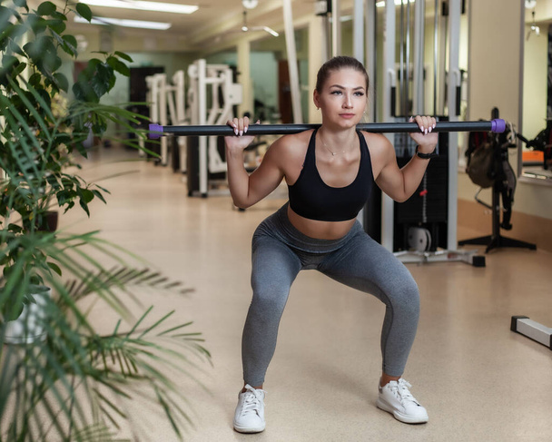 Slim fit nő sportruházat csinál guggolás gyakorlat egy súlyzóval a vállán az edzőteremben. Egészséges életmód koncepció. - Fotó, kép